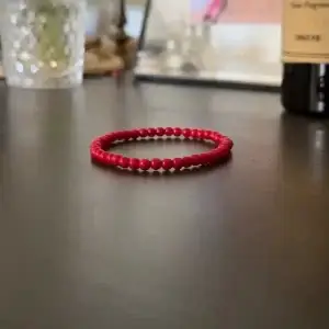 Pulsera roja de jade natural hecha a mano sobre fondo neutro, ideal para protección energética y chakra raíz